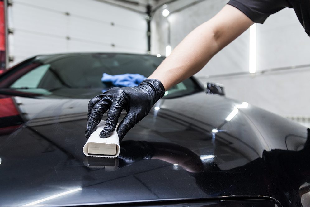 The process of applying a nano-ceramic coating on the car's hood by a male worker with a sponge and special chemical composition to protect the paint on the body from scratches, chips and damage.